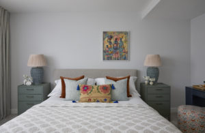 Bedroom in a renovated period home with a colourful painting, pleated lampshades, green bedside chests and embroidered cushions